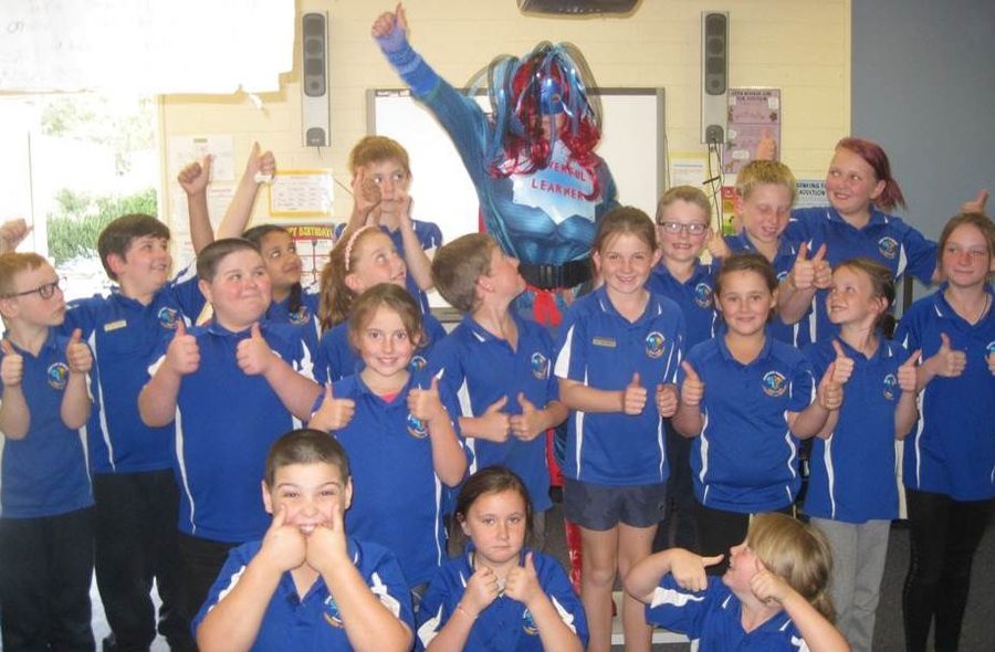 Class of happy students with a teacher dressed as a superhero